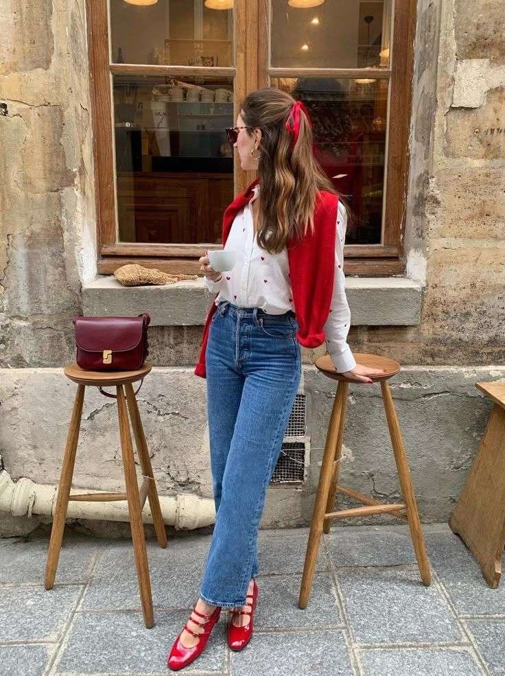 This Parisian-inspired spring look is commonly referred to as French Girl Chic. [20, 25] A crisp, white button-down shirt featuring a playful all-over red heart embroidery.  High-waisted, straight-leg jeans in a classic blue wash, providing a structured yet effortless silhouette. Coordinated red accents through patent leather Mary Jane flats and a matching sweater draped over the shoulders.