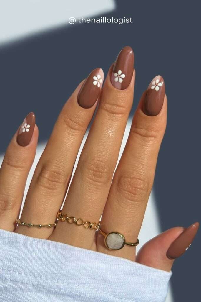 For a softer, more whimsical fall nail aesthetic, brown nails with white daisy art are having a major moment. The contrast between the warm earthy brown base and tiny white florals creates a look that's both cozy and cute — perfect for the cottagecore fall aesthetic trending in 2026.