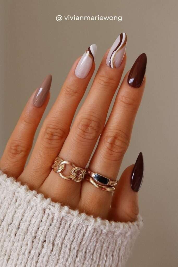 Abstract swirl and line nail art is one of the biggest fall nail art trends for 2026. Brown, cream, and gold lines create painterly movement on a neutral base — giving serious art gallery energy.