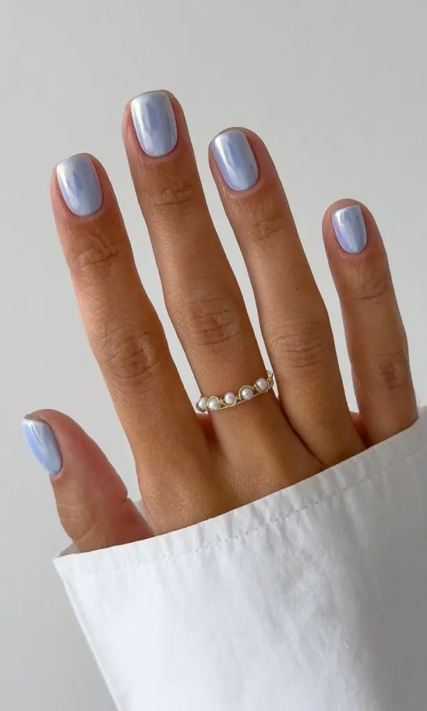 This chic look pairs a modern, short squoval shape with a refreshing, pale baby-blue base coat. It is layered with a fine white-silver chrome powder that gives the nails a metallic, liquid-pearl finish perfect for cooling down a hot July day. 
