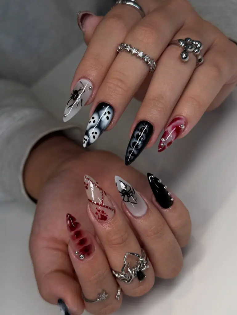 Gothic Spider & Haunted House Halloween Nails. For those who love dramatic Halloween nail art, this long stiletto set delivers maximum impact. The black-and-white color palette features spiders, ghost silhouettes, stitched details, blood-inspired accents, and crystal embellishments.