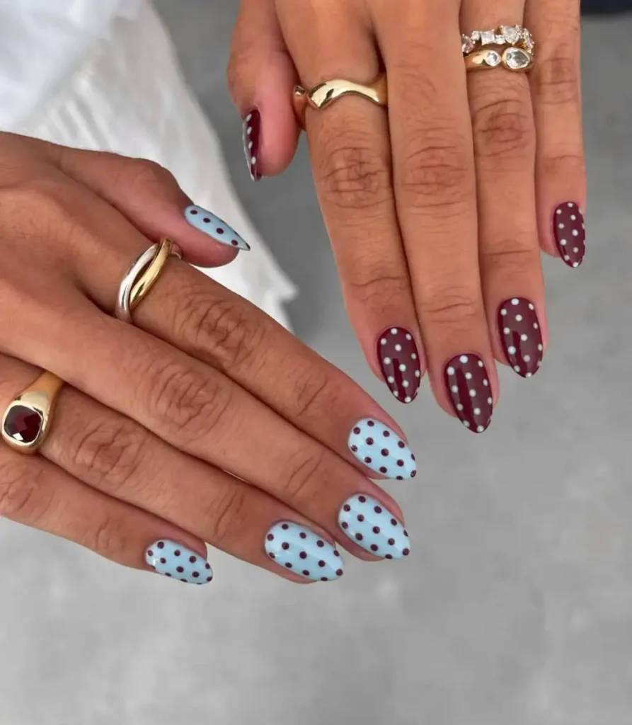 Two hands showing a dusty blue manicure with brown polka dots next to a burgundy manicure with white polka dots.