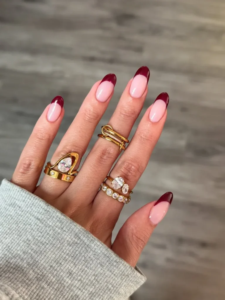 Long oval nails with a pale pink base and a wide, dramatic burgundy French tip.