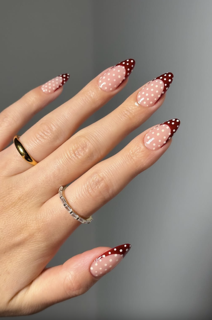 Long almond nails with a sheer nude base and burgundy French tips accented with cream polka dots.