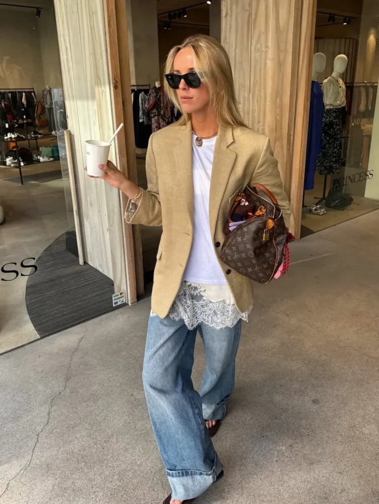 Woman in a tan blazer with a lace slip peeking out under a white tee and wide-leg jeans