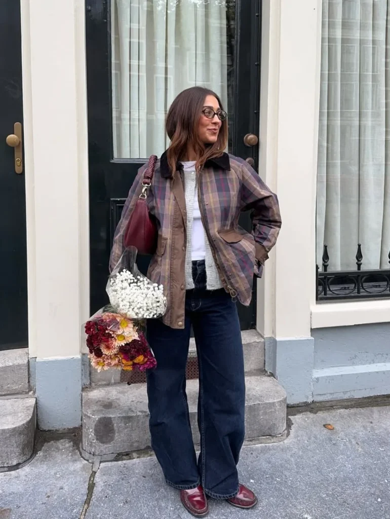 Woman in a plaid barn jacket and cream cardigan holding a bouquet of flowers on a city street