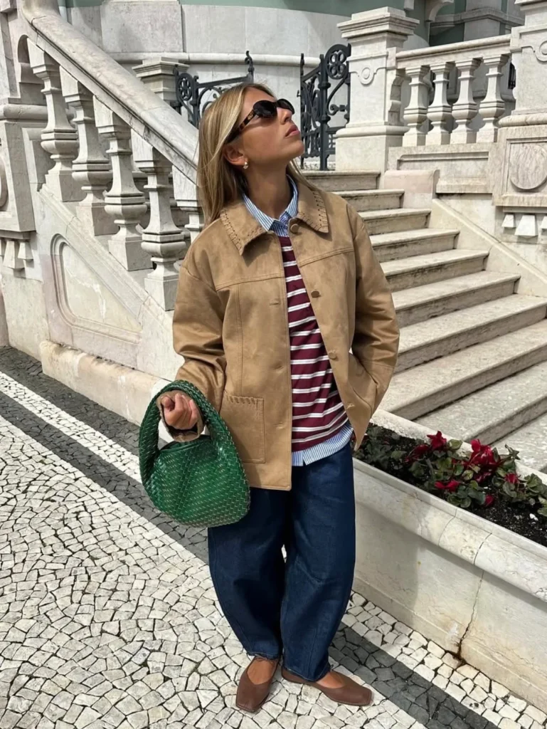Woman on stone steps wearing a tan suede jacket over layered burgundy and blue striped tops