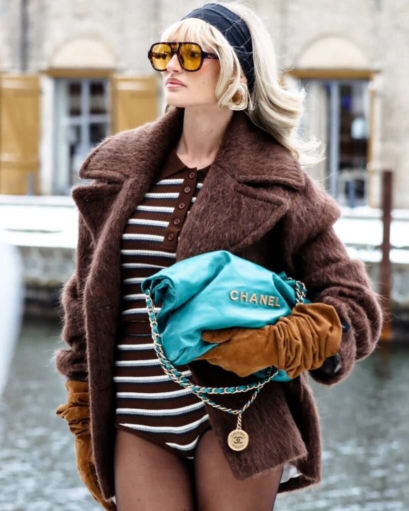 Close-up of a woman in an oversized brown teddy coat holding a teal quilted bag.