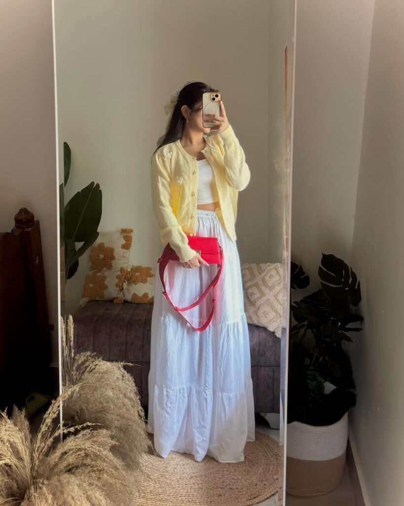 Woman in a yellow cardigan and white tiered maxi skirt taking a mirror selfie