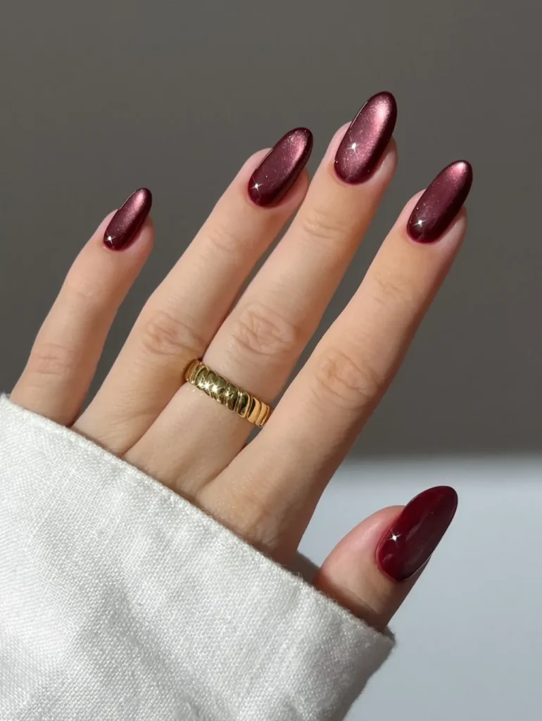 Long almond nails in a deep wine-toned cat-eye manicure with a shimmering light-catching finish.