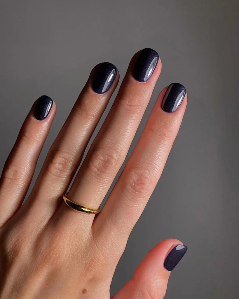 Short round nails painted a solid deep midnight blue with a fine shimmer finish.