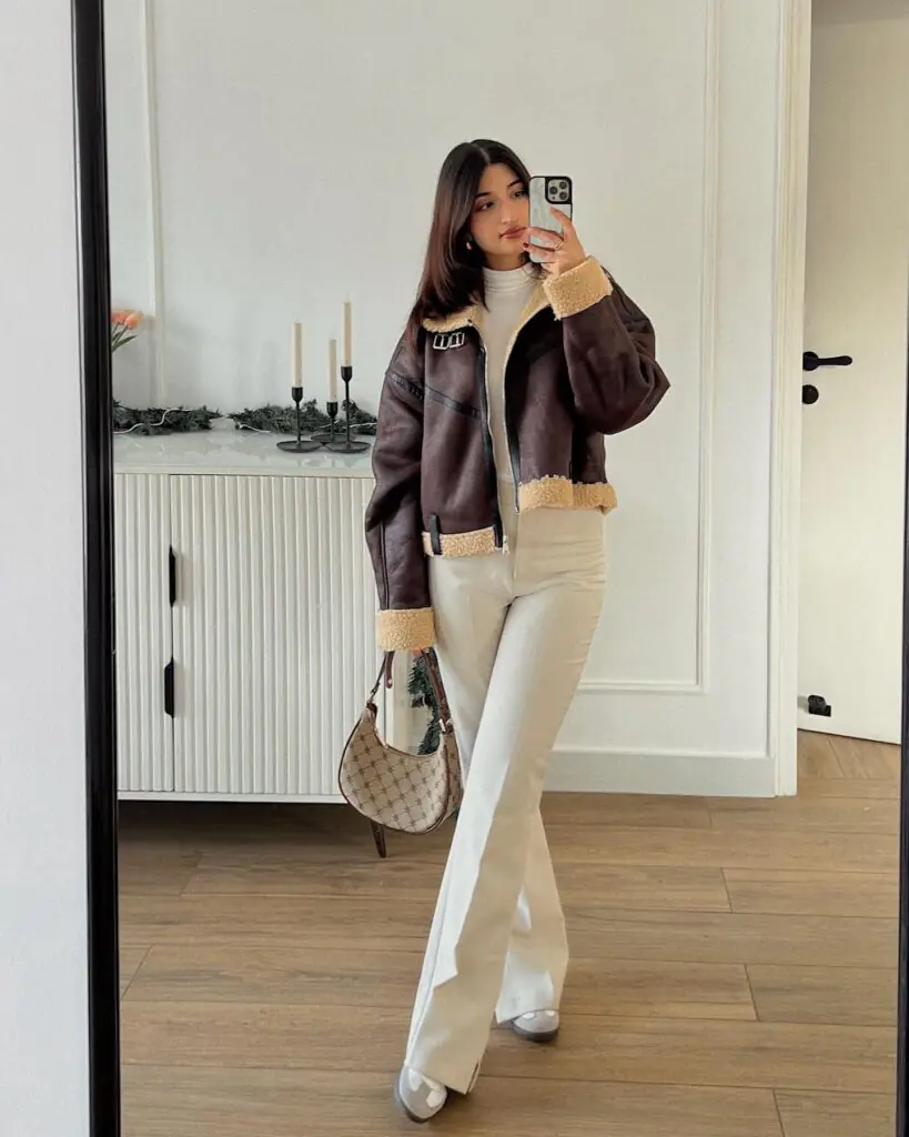 The classic shearling aviator jacket gets a fresh, contemporary update with a sharp, cropped silhouette.
Rich chocolate brown leather contrasts cleanly with warm, honeyed cream trims along the structured edges.
High-waisted off-white trousers elongate the frame, creating a clean and sophisticated color story.
A vintage-inspired monogram shoulder bag adds a subtle nod to heritage luxury accessories.
Grounded by sleek sneakers, it is the quintessential uniform for running errands in style.