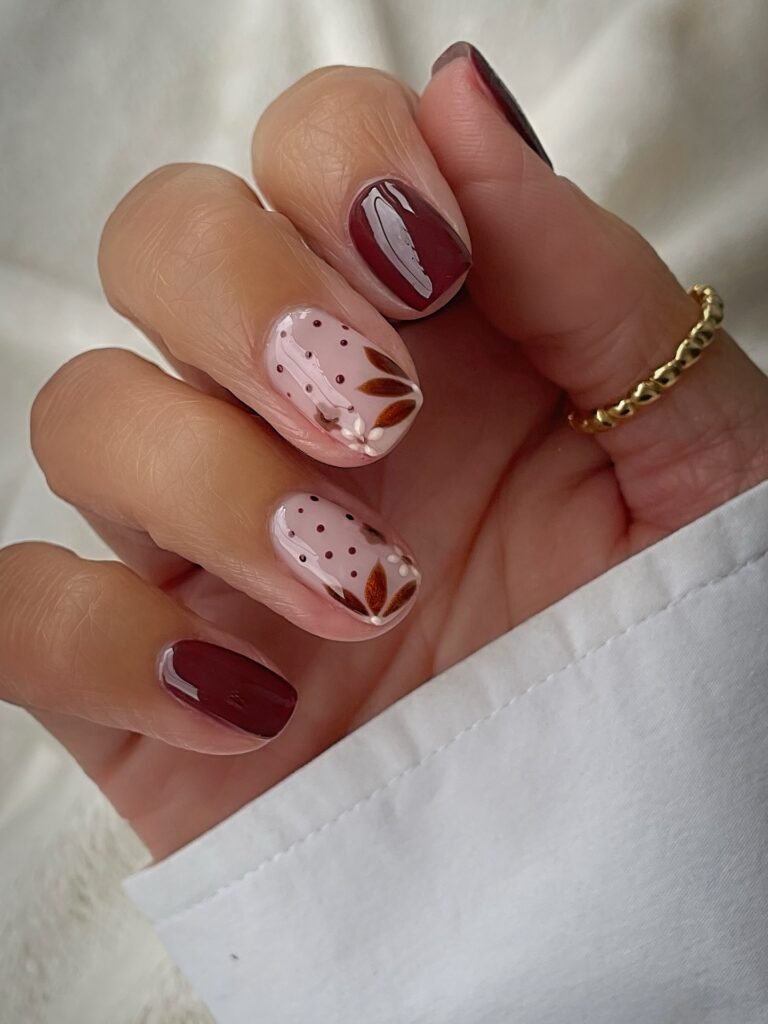 This short set mixes two solid burgundy nails with two sheer pink accents. Each has scattered brown dots, copper leaf petals and a tiny white flower. It’s delicate and detailed, and the short length keeps it from feeling fussy.