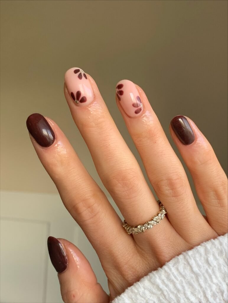 This one is for the reader who wants nail art but is nervous about it. Two nails in glossy espresso frame two sheer blush nails with burgundy petals and a tiny gem at the base. It’s the right amount of detail: you notice it up close, but it won’t clash with anything