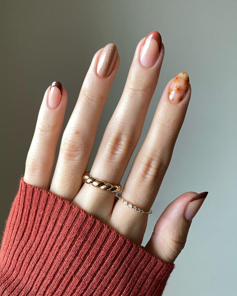 This set is a little mix-and-match: a chocolate French tip, a copper holographic shimmer, a rust-red V tip and one orange flower accent. It shouldn’t work on paper, but it does because every colour sits in the same warm family.
